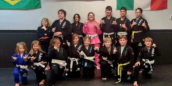 Group of young martial artists posing in gis with various belts indoors.