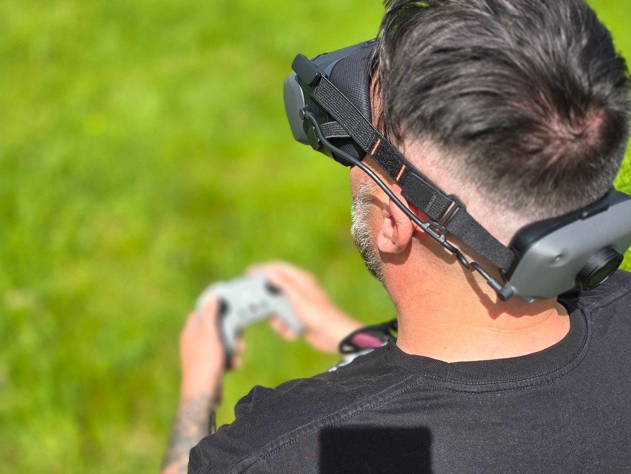 Man wearing VR headset playing with a controller outdoors on grass.