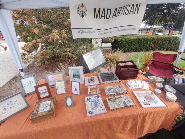Art display booth with handmade crafts and framed art.