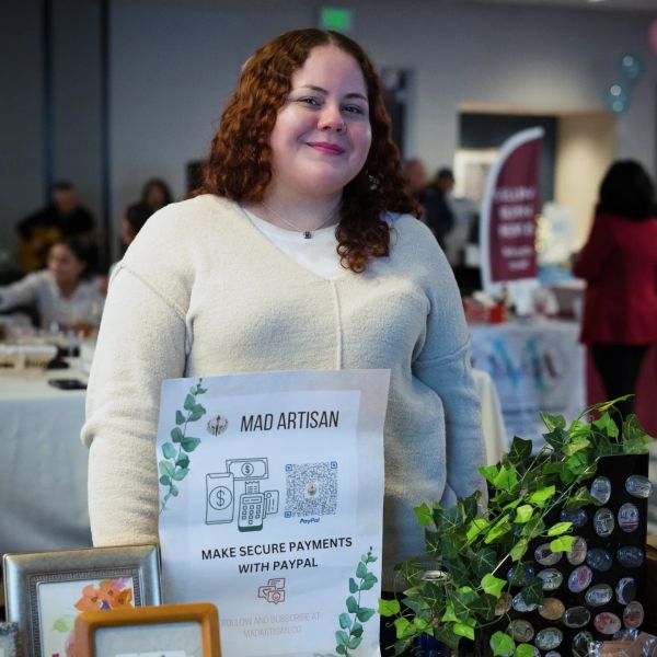 Woman smiling at a craft fair booth with a sign for secure PayPal payments.