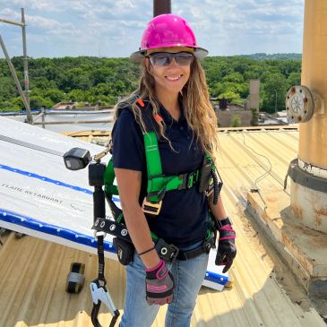Woman in pink hard hat on a rooftop with safety gear.