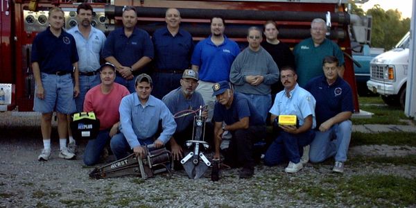A group of firefighters posing with equipment in front of a fire truck.