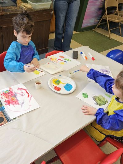 Two children painting at a table with colorful paints.