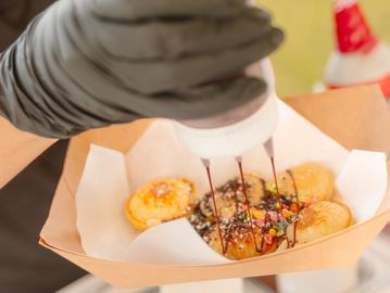 Person drizzling sauce on a tray of takoyaki balls.