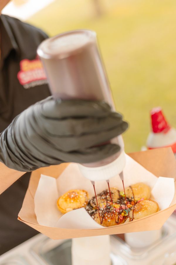 Gloved hand drizzling chocolate sauce on pancake bites.