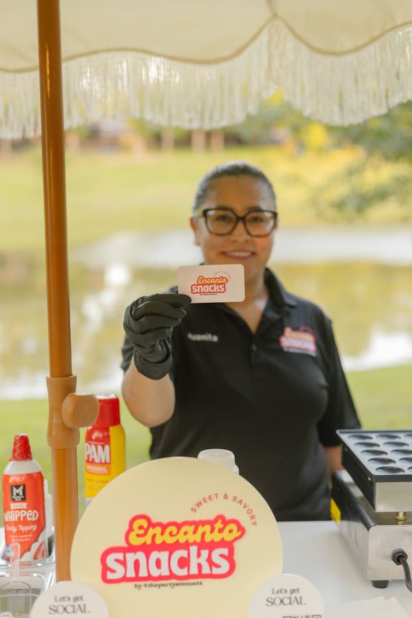 Vendor proudly holds an Encanto Snacks card at an outdoor booth.