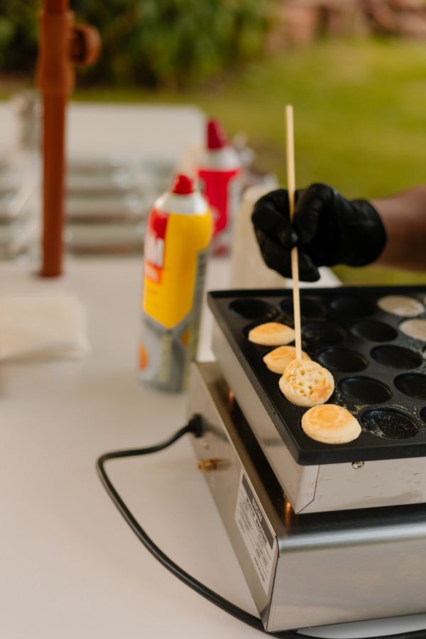 Making small pancakes on a specialized griddle with a wooden skewer.