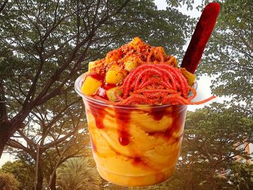 A vibrant mango sorbet topped with spicy chili and tamarind candy in a clear cup.