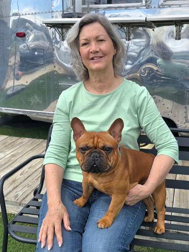 A woman in a green shirt sitting on a bench with a brown French Bulldog.