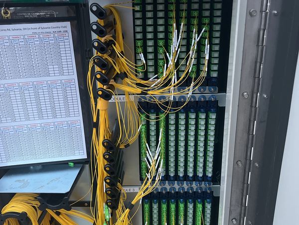 Fiber optic splice cabinet with organized yellow cables and modules.