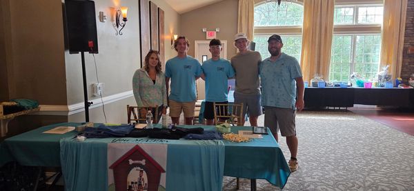 Group of people standing behind a table with promotional materials in a bright room.