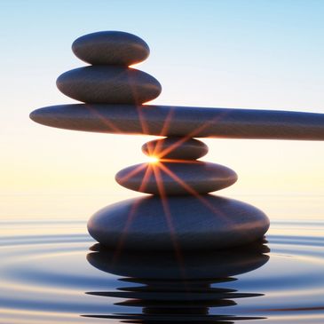 Balancing rocks on rippling water with the sun in the background