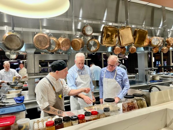 Three men in aprons discussing in a commercial kitchen.