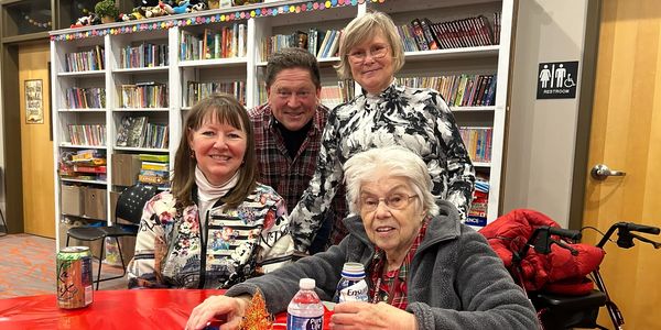 Four people smiling at a table in a cozy library setting with drinks and a walker.
