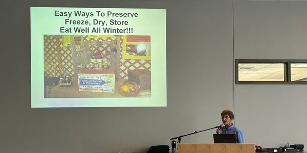 Woman giving a presentation on food preservation with jars displayed.