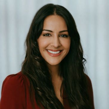 Smiling woman with long dark hair and a red blouse against a light background.