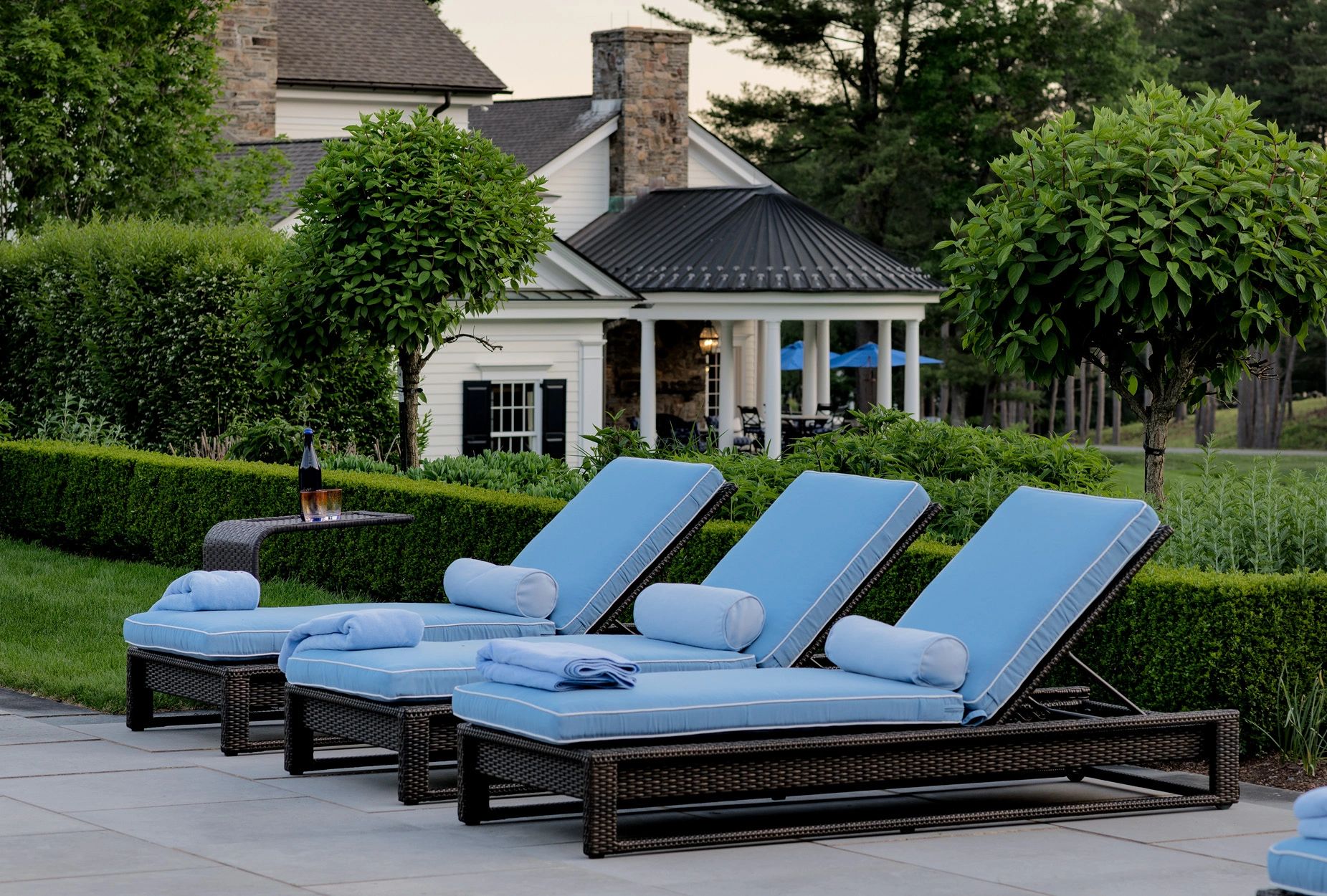 Estate garden with blue lounge chairs by a poolside with a greenery backdrop.