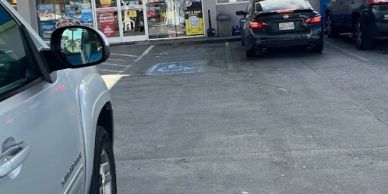 Handicapped parking space in front of a store with vehicles nearby.