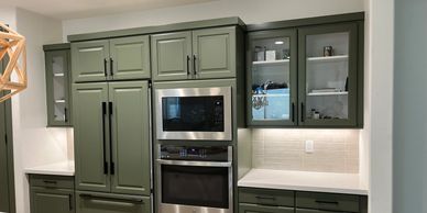 Modern kitchen with green cabinets and stainless steel appliances.
