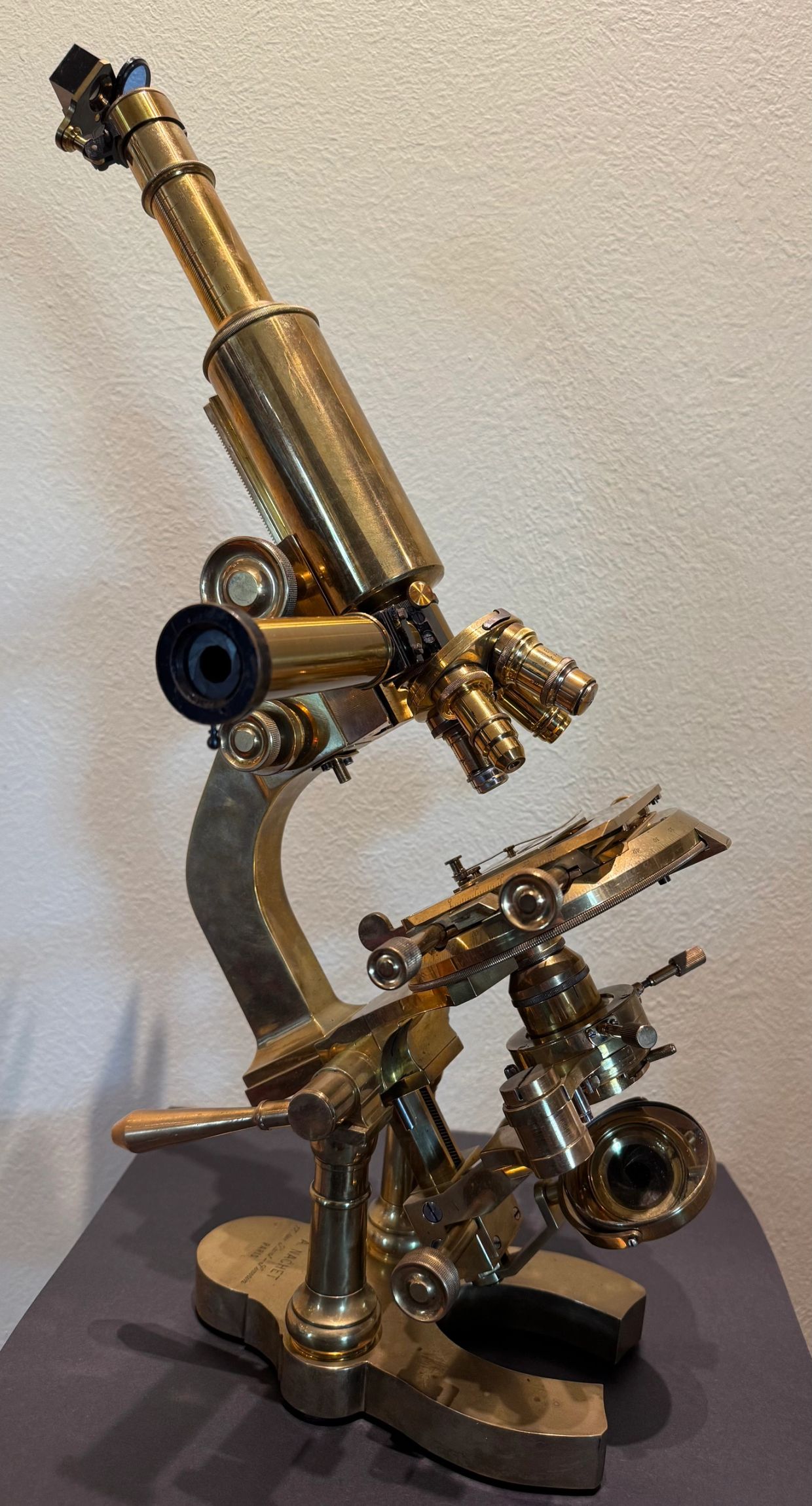 Vintage brass microscope against a plain wall.