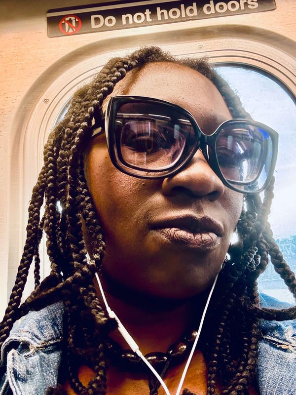 Close-up of a woman with braided hair and large sunglasses on public transport.