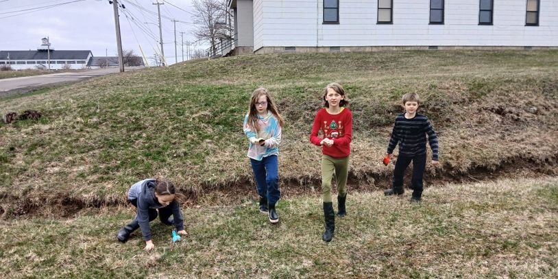 Four children playing outside on a grassy hill near a house.