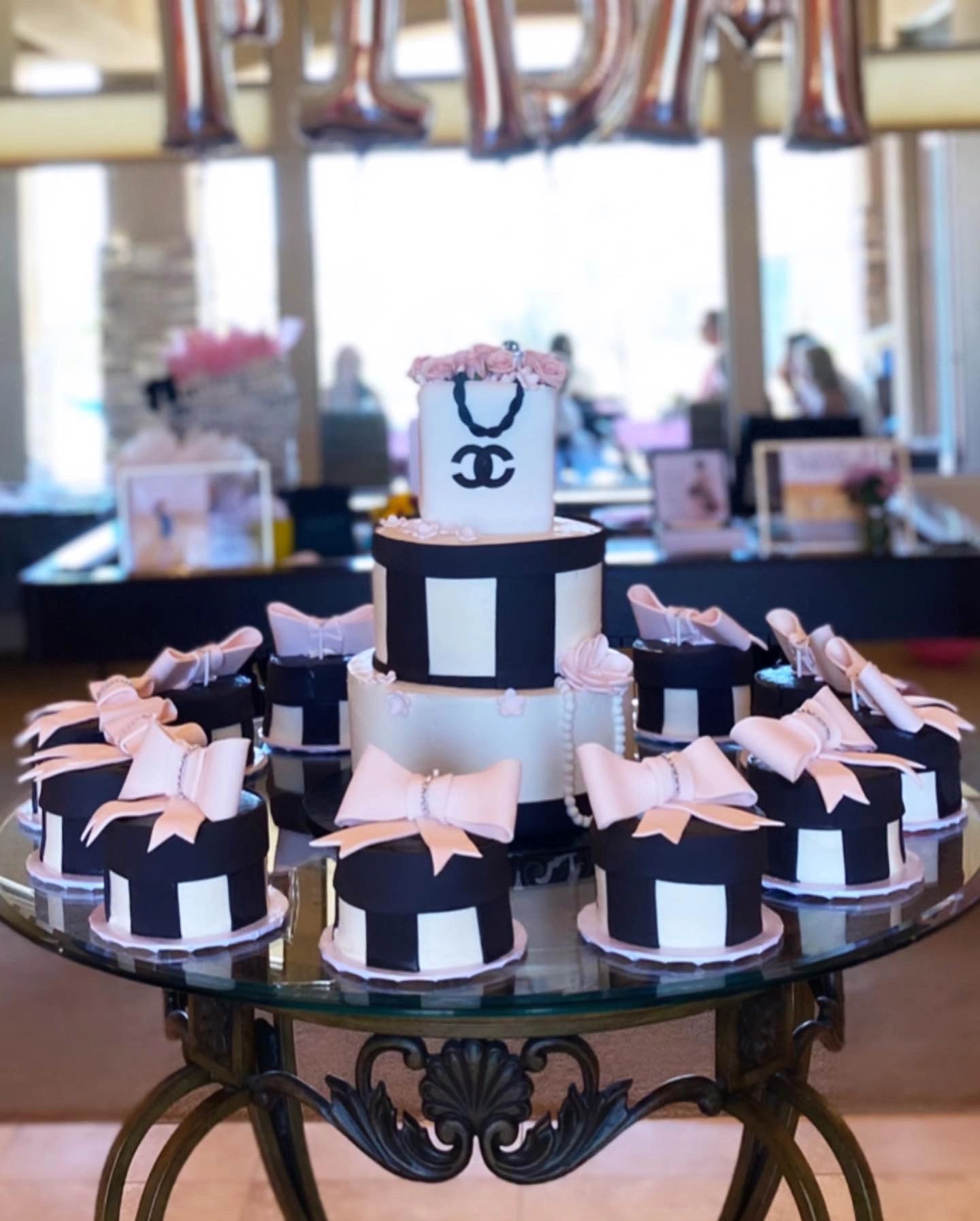 Elegant black and white tiered cake with pink bows and roses on a glass table.