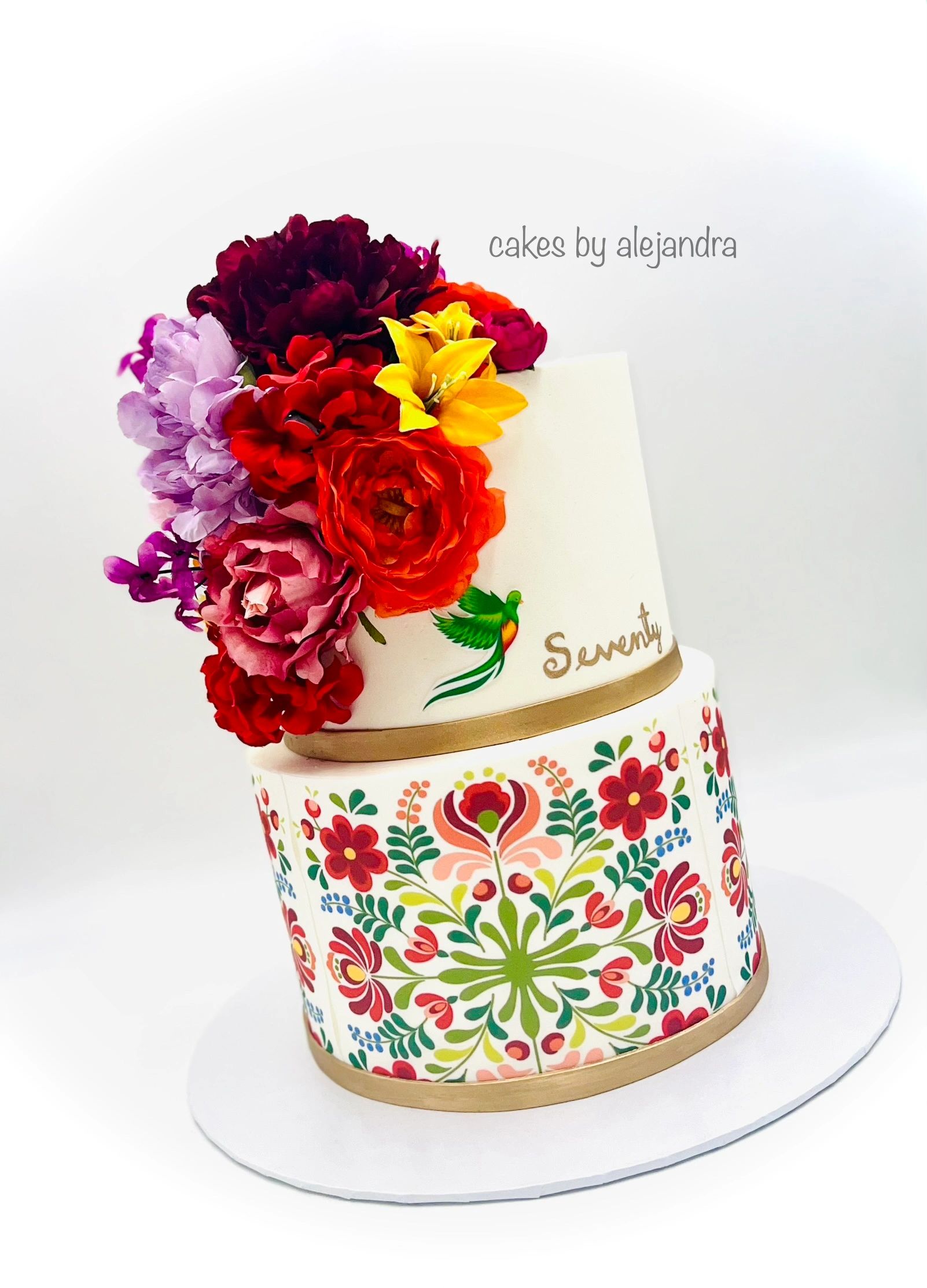 Elegant two-tier cake with vibrant floral decorations and intricate patterns.