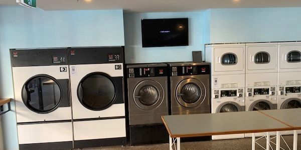 Modern laundromat with multiple washing and drying machines and folding tables.