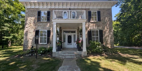 Historic stone house with white trim and black shutters on a sunny day.