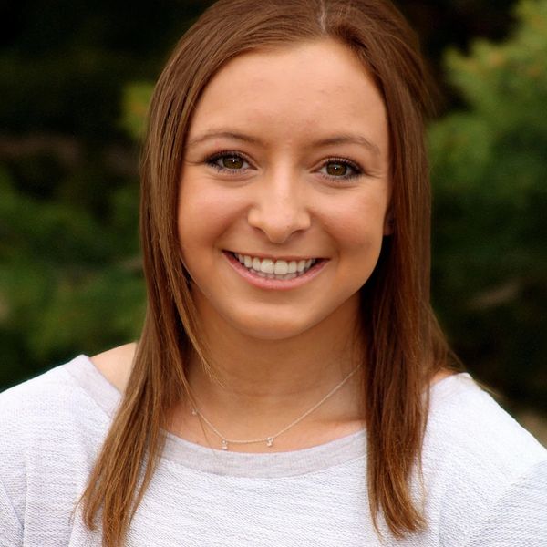 Young woman with brown hair smiling outdoors against a blurred green background.