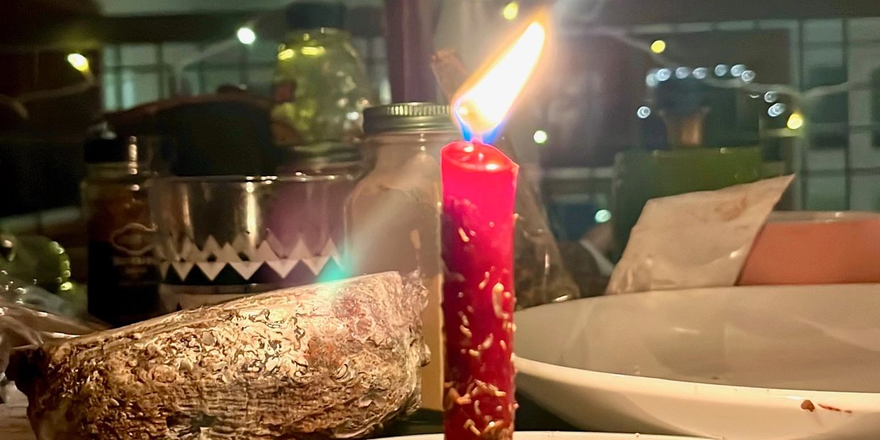 A lit red candle on a table with various jars and dishes in the background.