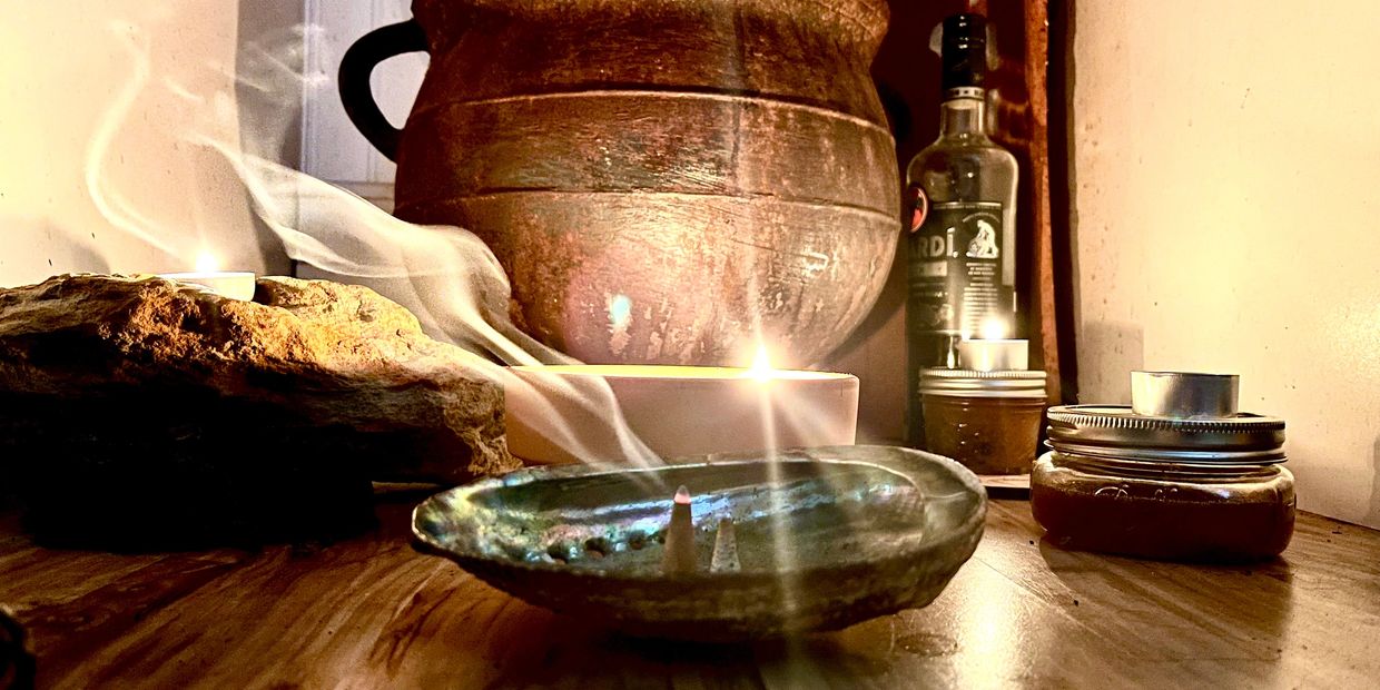Incense burning on a rustic ceramic dish amidst candles and a large clay pot.