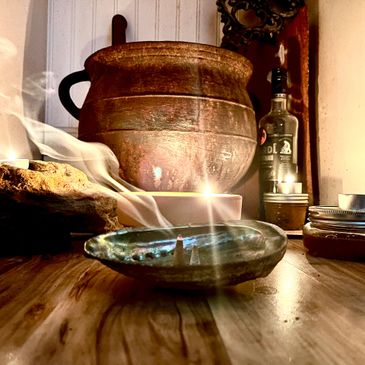 A rustic oil lamp burning on a wooden surface with a large clay pot in the background.