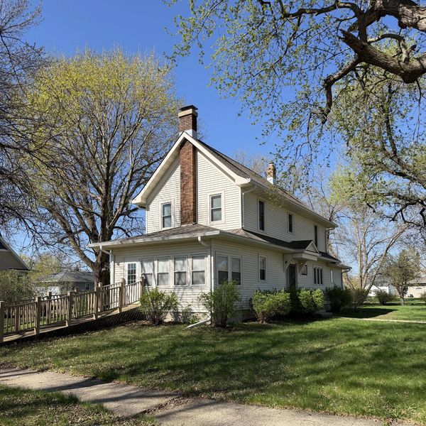 A two-story white house with a wooden ramp and large trees in the yard.