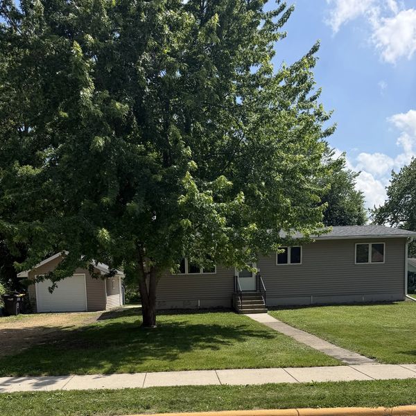 A suburban house with a large tree and detached garage on a sunny day.