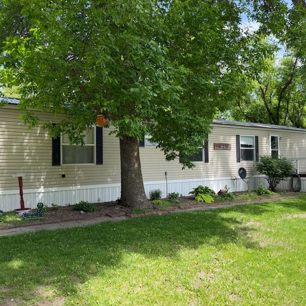 A beige mobile home with a large tree and green lawn in front.