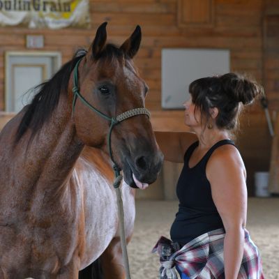 Woman standing beside a brown horse indoors.