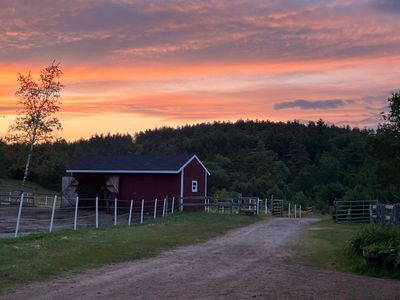 A rustic red barn at sunset with a dirt path and fenced grassy area.