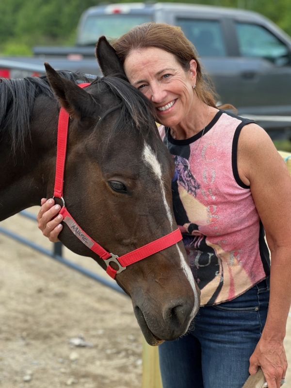 Woman smiling with a horse wearing a red halter.
