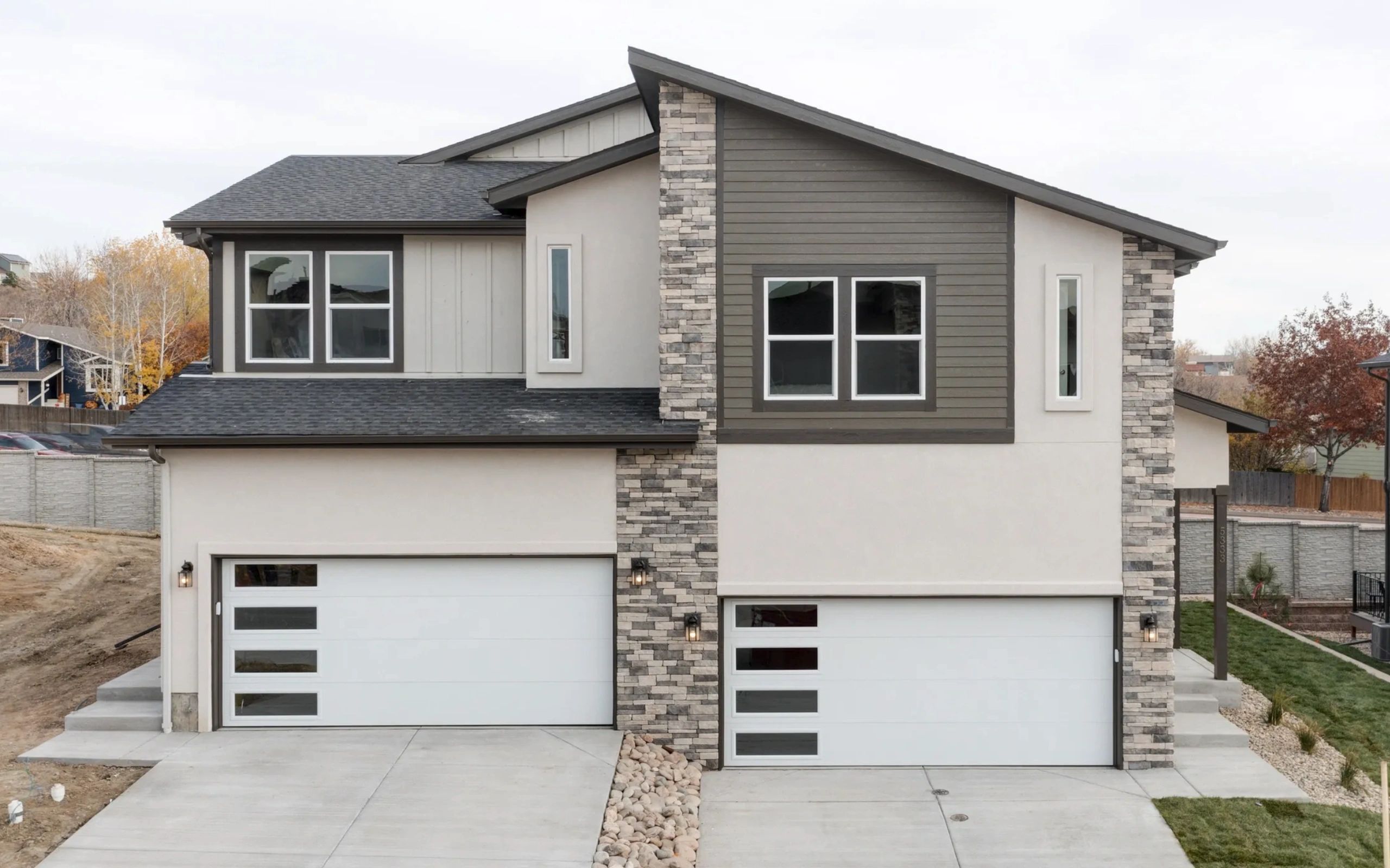 Modern duplex with stone accents and white garage doors.