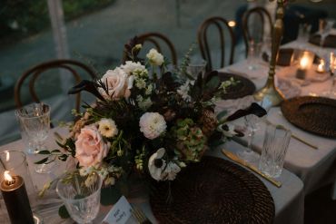 Elegant floral centerpiece with soft pink and white flowers on a candlelit dinner table.