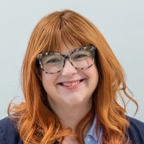 Smiling woman with red hair and glasses.