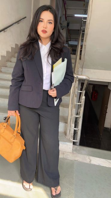 Woman in formal attire holding a handbag and documents.