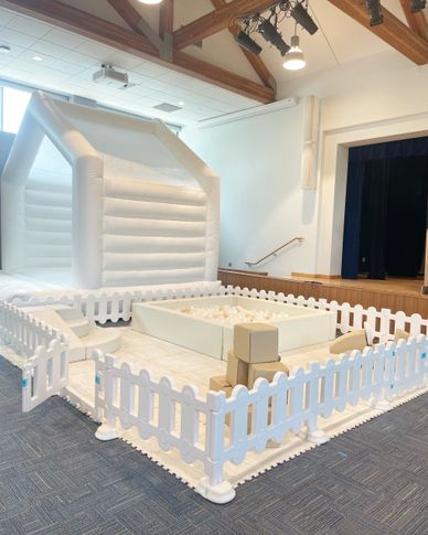 Indoor white inflatable playhouse and ball pit enclosed by white picket fencing.