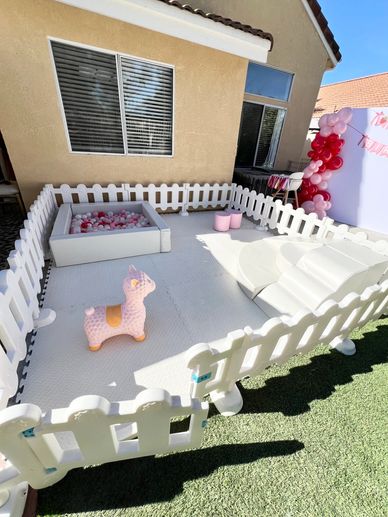 Outdoor playpen with white fencing, soft mat, and toys for kids.
