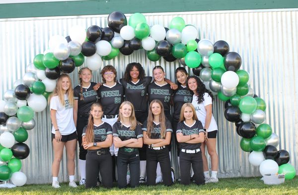 Girls' softball team posing under a balloon arch.