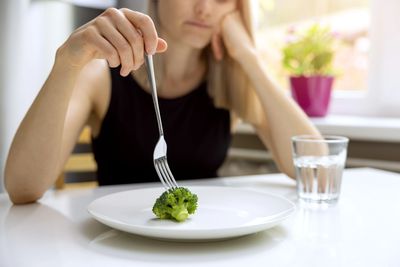 Woman putting fork in broccoli.  Seeking eating disorder therapy.