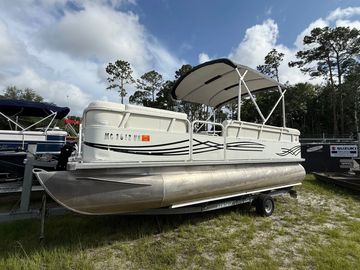 Pontoon boat parked on trailer near trees.