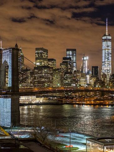 Night view of a city skyline with a lit suspension bridge over water.